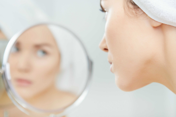 kobieta przyglądająca się swojej twarzy w lustrze.